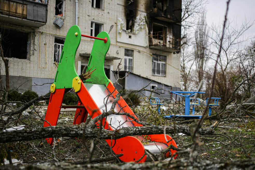 Дитячий майданчик на фоні обстріляної російськими військовими багатоповерхівки в Тростянці, квітень 2022 року. Фото: Стас Юрченко, Ґрати